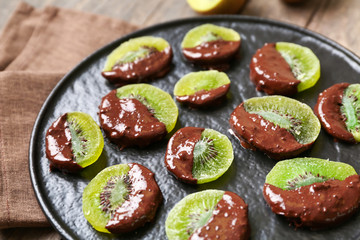 Tasty chocolate covered kiwi on plate, closeup