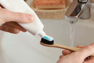 Fototapeta na wymiar Woman squeezing toothpaste on brush in bathroom, closeup