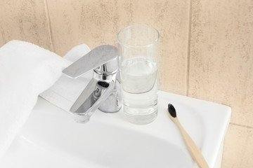 Toothbrush with glass of water and towel on sink in bathroom