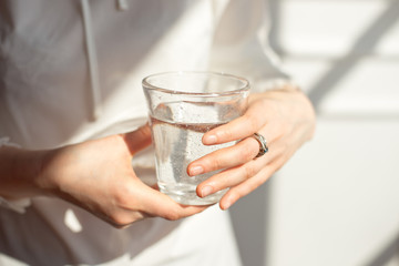 Close-up girl hands in the office stands in the sunlight holding a glass of clean water in between work