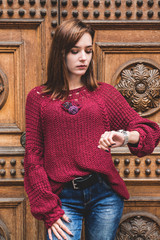 Fototapeta na wymiar The beautiful model poses in a knitted pullover of red color against the background of a wooden wall