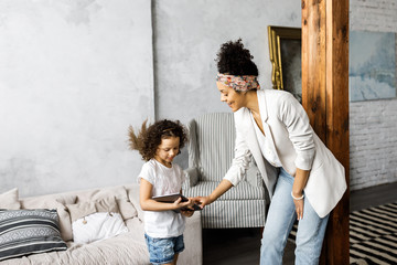 A cute mother and daughter talk and look at the tablet while standing in the living room