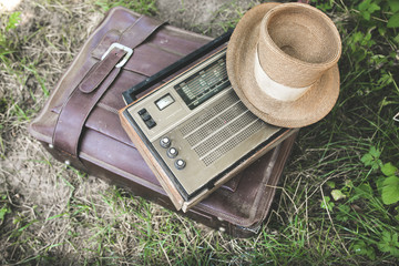 Retro radio and straw hat are lying on the old leather suitcase. Travel lifestyle concept. Vintage...