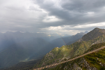 Suspension trail over a precipice and a rainbow in the Caucasus Mountains under a stormy sky, Krasnodar region, Russia