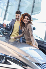 selective focus of cheerful curly woman smiling near excited man in glasses looking at car