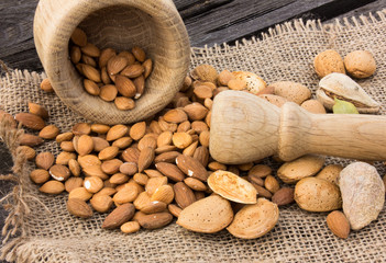 Almonds in a wooden cup on a burlap cloth background. Golden almond closeup in dark brown cup