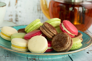 Dessert macaroons on a plate with a kettle of tea