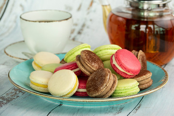 Dessert macaroons on a plate with a kettle of tea