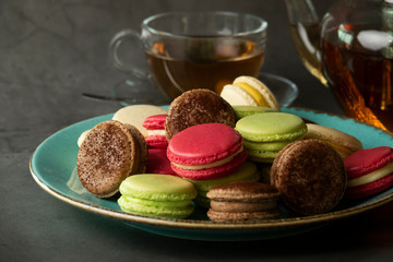 Dessert macaroons on a plate with a kettle of tea