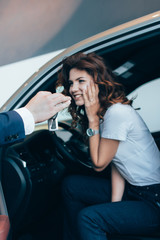 cropped view of car dealer giving keys to excited successful woman sitting in car