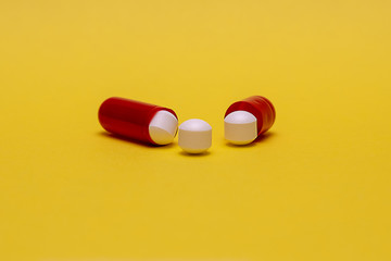 Offene rote Tablettenkapsel und drei weiße Tabletten auf gelben Untergrund