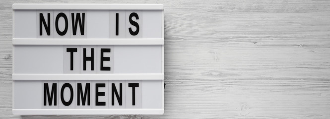 Obraz premium 'Now is the moment' words on modern board on a white wooden background, top view. From above, flat lay, overhead. Copy space.