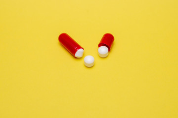 Offene rote Tablettenkapsel und drei weiße Tabletten auf gelben Untergrund