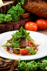 Grilled meat with grilled vegetables and fresh lettuce in teriyaki sauce on a white plate on a dark wooden background, decorated with fresh vegetables and greens. Close-up