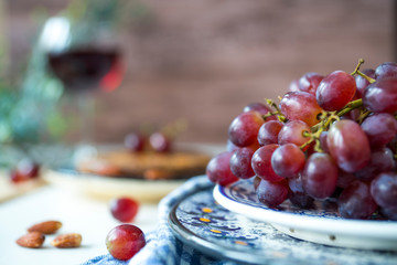 close up blue plate with bunch of red grapes,  wine, white table, wooden background
