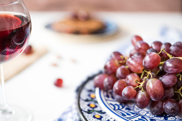 close up blue plate with bunch of red grapes,  wine, white table, wooden background