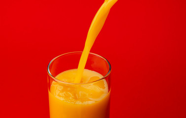 Orange juice pouring into glass, isolated on red color background, with copy space
