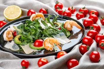Salad with shrimp, cherry tomatoes, avocado and arugula on textile background