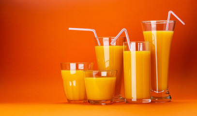 Glasses of orange juice isolated on colour orange background with copy space for text, fresh citrus cocktail