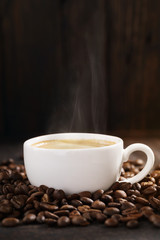 Cup of hot coffee with steam and roasted coffee beans.