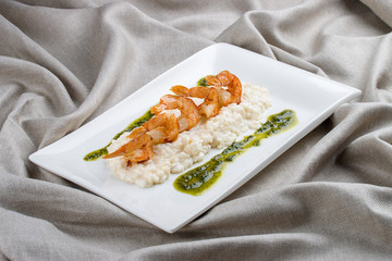 Shrimps with risotto and pesto on a white plate, on a textile background