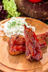 grilled veal ribs on a wooden round board against the background of fresh vegetables. close-up. space