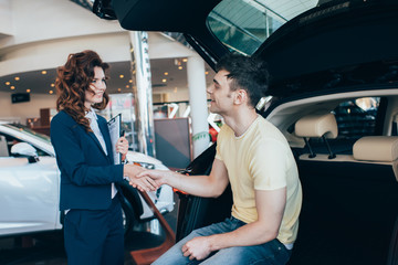 selective focus of happy man and pretty car dealer shaking hands in car showroom