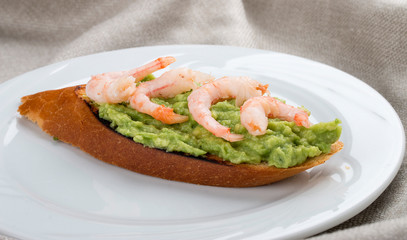 Bruschetta with shrimp and avocado mousse on a white plate, on a textile background