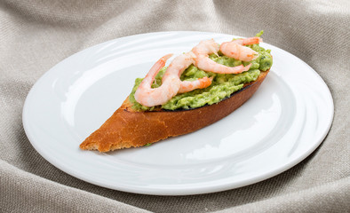 Bruschetta with shrimp and avocado mousse on a white plate, on a textile background
