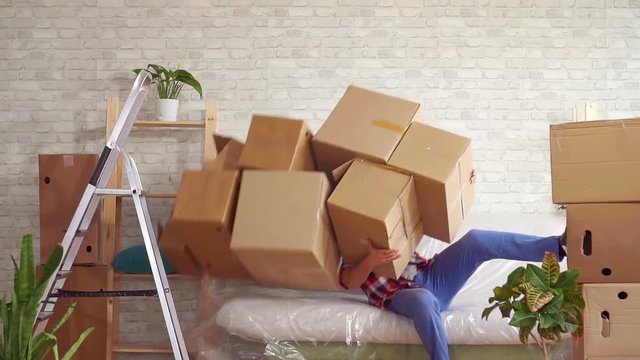 Man with heavy boxes in his hands loses his balance and falls on the sofa slow mo