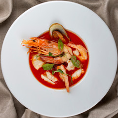 French bouillabaisse fish soup with shrimp, mussels and scallop. In a white plate on a textile background. Top view