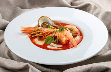 French bouillabaisse fish soup with shrimp, mussels and scallop. In a white plate on a textile background