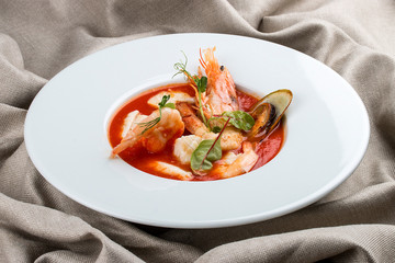 French bouillabaisse fish soup with shrimp, mussels and scallop. In a white plate on a textile background