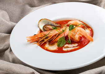 French bouillabaisse fish soup with shrimp, mussels and scallop. In a white plate on a textile...