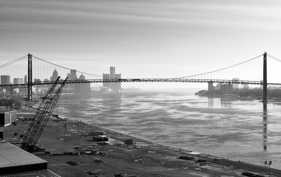 A Detroit view from the river of the skyline and skyscrapers in the winter in monochrome with a crane and suspension bridge at sunrise.