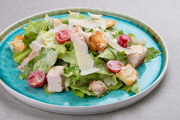 Caesar salad with chicken, Parmesan and cherry tomatoes. In a blue plate on a textile background