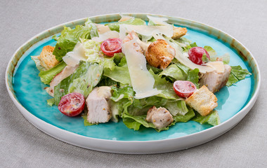 Caesar salad with chicken, Parmesan and cherry tomatoes. In a blue plate on a textile background