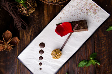 Beautiful chocolate cake, decorated with mint on a square white plate on a brown rustic background. Space