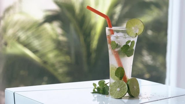 thin transparent curtain swings in light wind and mojito cocktail stands on white clean terrace table