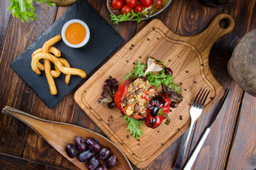 Grilled red bell pepper stuffed with meat and rice, served fresh lettuce on a light wooden board. And Churros with sauce on a black plate on a dark wooden background with fresh vegetables. Close up