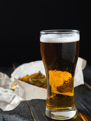A glass of cold light beer on a wooden table and fries by country