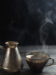 Freshly brewed coffee in jezve on a dark background. The hot steam from the drink