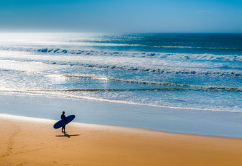 Fototapeta na wymiar Lone surfer on beach watching the incoming waves