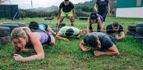Group of participants in an obstacle course crawling under electrified cables