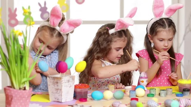 Happy children wearing bunny ears painting eggs on Easter day. Little girls preparing for the Easter.