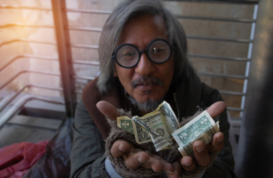 Homeless man is sitting down on walkway in town. He is receive dollar.He is  hoping to have the better life. poverty, despair, Photo Sympathetic and hope concept. - Powered by Adobe