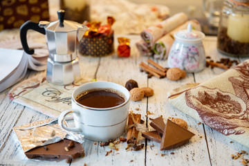 Coffee mug, chocolate, coffee beans, cinnamon sticks and spices on white wooden table. Good morning breakfast or coffee break set background.