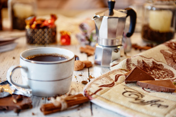 Naklejka na ściany i meble Coffee mug, chocolate, coffee beans, cinnamon sticks and spices on white wooden table. Good morning breakfast or coffee break set background.