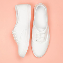 White female sneakers on coral background. Flat lay, top view minimal style