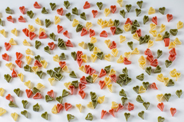 on a white background pasta in the form of hearts (red, green and yellow), texture over the whole background